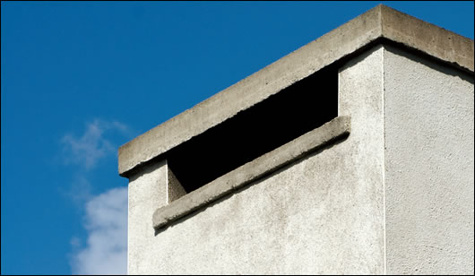 the chimneys rise on either end of the house, there to facilitate the wood pellet stoves, while also providing one of the house’s most striking features